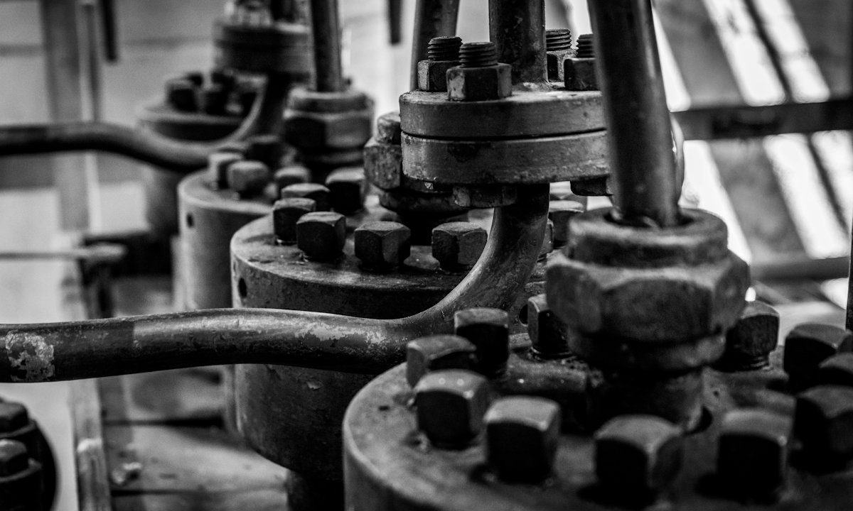 Close-up of heavy industrial valves and bolted pipe flanges, in black and white